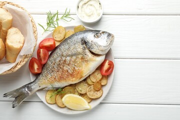 Homemade seafood dish. Tasty roasted dorado fish served with vegetables and sauce on white wooden table, flat lay. Space for text