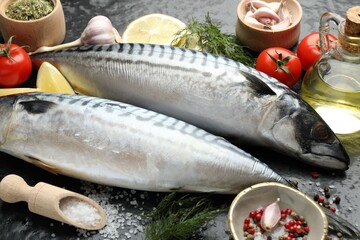 Fresh raw mackerels and spices on black table, closeup. Seafood delicacies