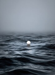Solitary white sphere floats on dark, wavy sea under a misty sky