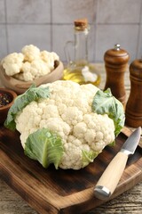 Fresh cauliflower with green leaves, spices and knife on wooden table, closeup