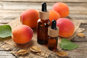 Aromatic essential oil in bottles, seeds, leaves and ripe apricots on wooden table, closeup