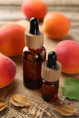 Aromatic essential oil in bottles, seeds and ripe apricots on wooden table, closeup
