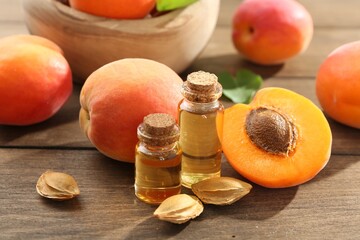 Aromatic essential oil in bottles, seeds and ripe apricots on wooden table, closeup
