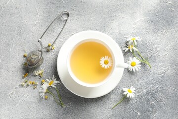 Tasty chamomile tea, infuser and flowers on light grey table, flat lay