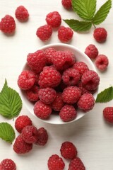 Tasty fresh ripe raspberries and leaves on white wooden table, flat lay