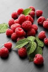 Tasty fresh ripe raspberries and leaves on black table, closeup