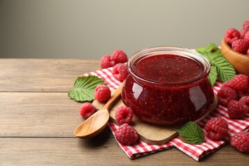 Tasty jam, fresh ripe raspberries and leaves on wooden table, closeup. Space for text