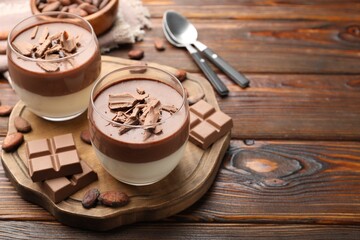 Delicious panna cotta in glasses, cocoa beans and chocolate pieces on wooden table. Space for text
