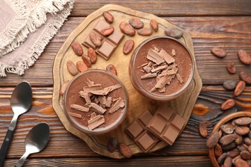 Delicious chocolate panna cotta in glasses, cocoa beans and chocolate pieces on wooden table, flat lay