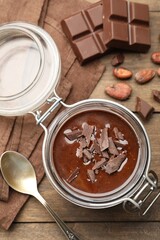Delicious chocolate panna cotta in glass jar, nuts and spoon on wooden table, flat lay