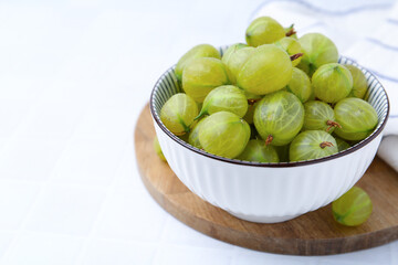Fresh green gooseberries in bowl on white table, closeup. Space for text