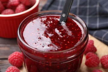 Sweet raspberry jam in glass jar and berries on table, closeup