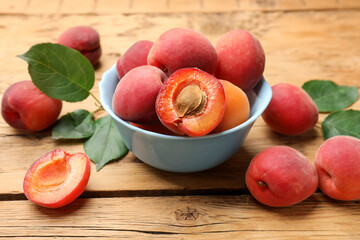 Many fresh apricots and green leaves on wooden table, closeup