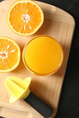 Fresh orange juice in glass, fruits and juicer on black table, top view