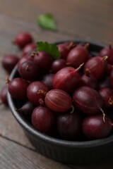 Ripe red gooseberries in bowl on wooden table, closeup