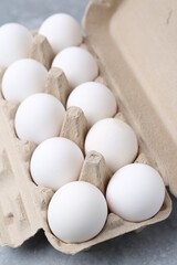 Raw chicken eggs in egg carton on grey table, closeup