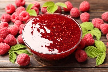 Delicious raspberry jam in glass bowl, fresh berries and mint on wooden table, closeup