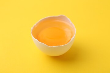 One broken chicken egg on yellow background, closeup