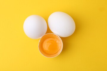 Whole and broken chicken eggs on yellow background, top view