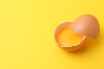 One broken chicken egg on yellow background, closeup. Space for text