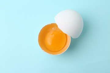 One broken chicken egg on light blue background, top view