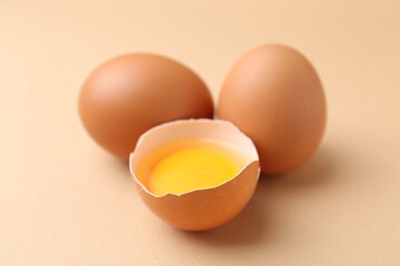 Whole and broken chicken eggs on beige background, closeup