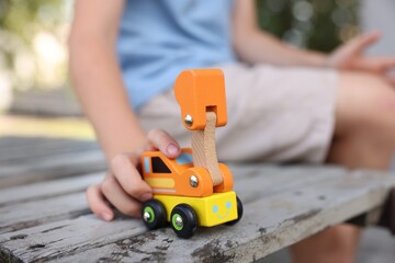 Little boy playing with toy car on wooden bench outdoors, closeup