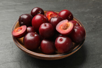 Ripe cherry plums in bowl on dark textured table, closeup