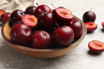 Whole, cut cherry plums in bowl on grey textured table, closeup