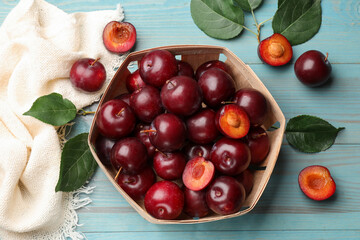 Whole, cut cherry plums, cloth and green leaves on light blue wooden table, flat lay