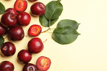 Whole, cut cherry plums and green leaves on light yellow background, flat lay. Space for text
