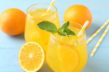 Refreshing soda water with orange slices in glasses, mint, fresh fruits and straws on light blue...