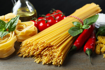 Different types of pasta and ingredients on wooden table, closeup