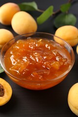 Tasty apricot jam and fresh fruits on black wooden table, closeup