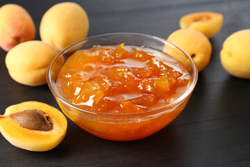 Tasty apricot jam and fresh fruits on black wooden table, closeup