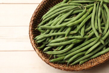 Fresh pea pods in wicker basket on light wooden table, top view. Space for text