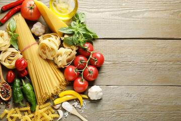 Different types of pasta and ingredients on wooden table, flat lay. Space for text