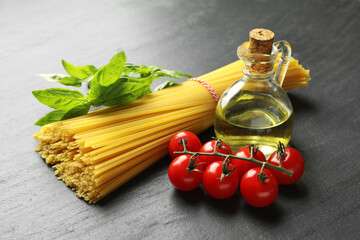Raw spaghetti pasta and different ingredients on black table, closeup