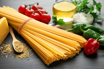 Raw spaghetti pasta, products and spices on black wooden table, closeup