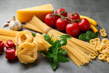 Different types of raw pasta and products on grey textured table, closeup