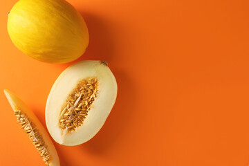 Whole and cut ripe melons on orange background, flat lay. Space for text