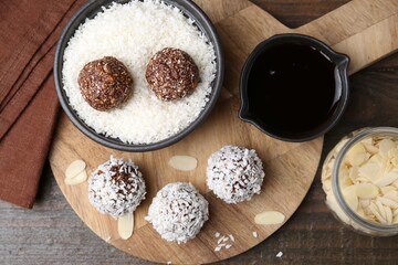 Delicious homemade candies with coconut flakes on wooden table, flat lay