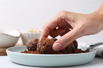 Woman making homemade candies with cocoa powder at white table, closeup