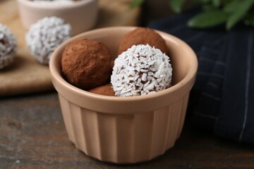 Delicious homemade candies with cocoa powder and coconut flakes in bowl on wooden table, closeup