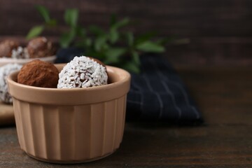 Delicious homemade candies with cocoa powder and coconut flakes in bowl on wooden table, closeup....
