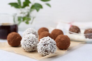 Delicious homemade candies with cocoa powder and coconut flakes on light table, closeup