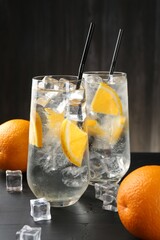 Refreshing soda water with orange slices and ice cubes on black wooden table, closeup