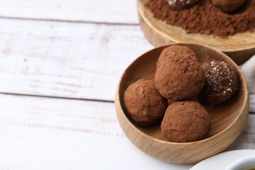 Delicious homemade candies with cocoa powder on white wooden table, closeup. Space for text