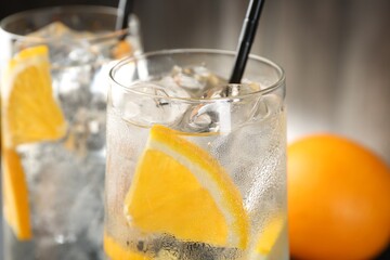 Refreshing soda water with orange slices and ice cubes in glasses on blurred background, closeup