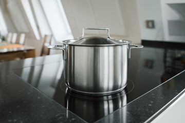 shiny stainless steel pot with a lid positioned on a modern induction cooktop, highlighting...